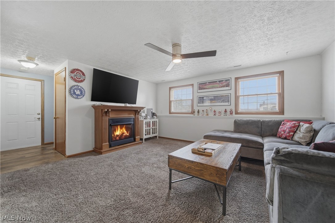 702 Perry Drive Northwest Canton, OH 44708 - Photo 28 of 46 Living room featuring a ceiling fan, a textured ceiling, a gas fireplace, and dark colored carpet
