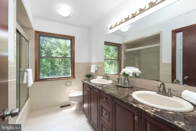 a bathroom with a granite countertop double vanity sink large mirror bathtub and toilet