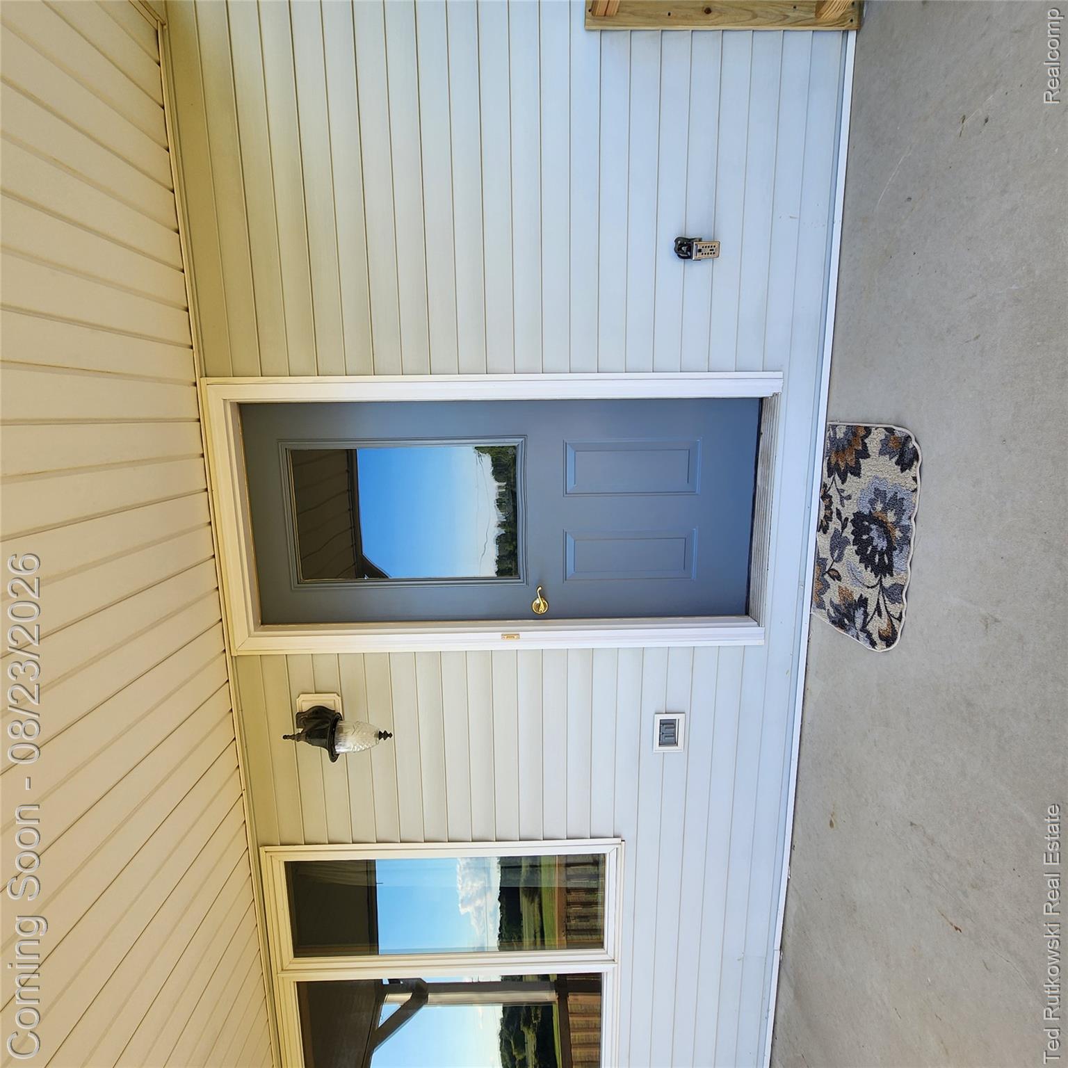 Covered concrete porch with light-toned siding, panel door featuring an integrated window.