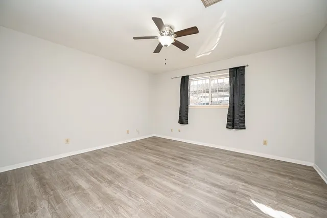 an empty room with wooden floor ceiling fan and windows