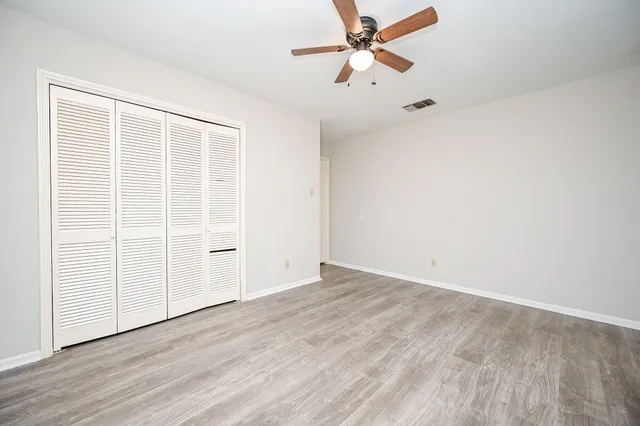 an empty room with wooden floor fan and windows