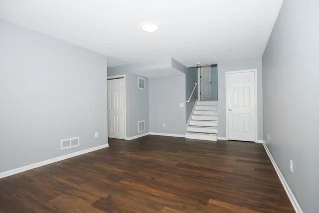 a view of an empty room with wooden floor and stairs