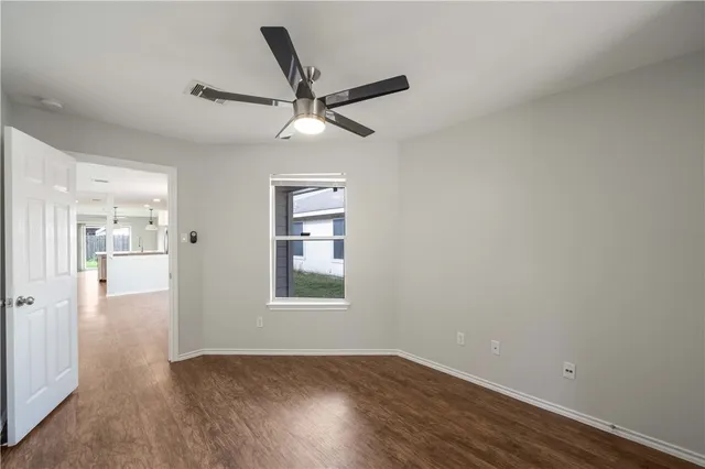 an empty room with wooden floor fan and windows