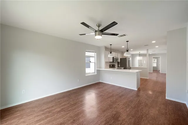 a view of an empty room and kitchen with wooden floor