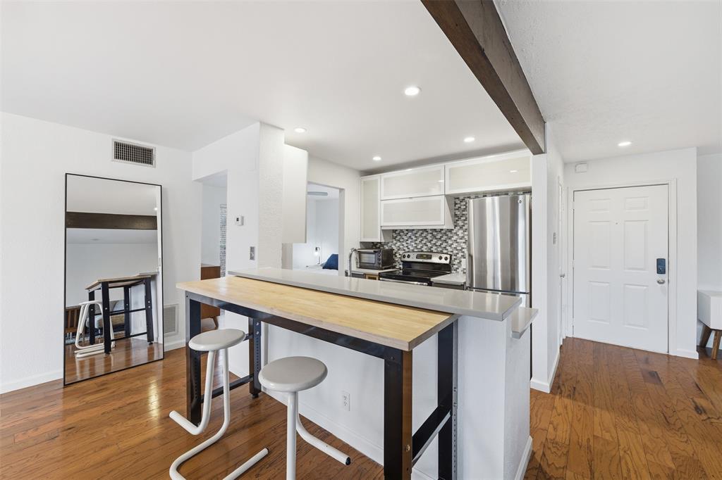4837 Cedar Springs Road, Unit 311 Dallas, TX 75219 - Photo 10 of 17 Kitchen with white cabinetry, dark wood-type flooring, a peninsula, stainless steel appliances, and backsplash