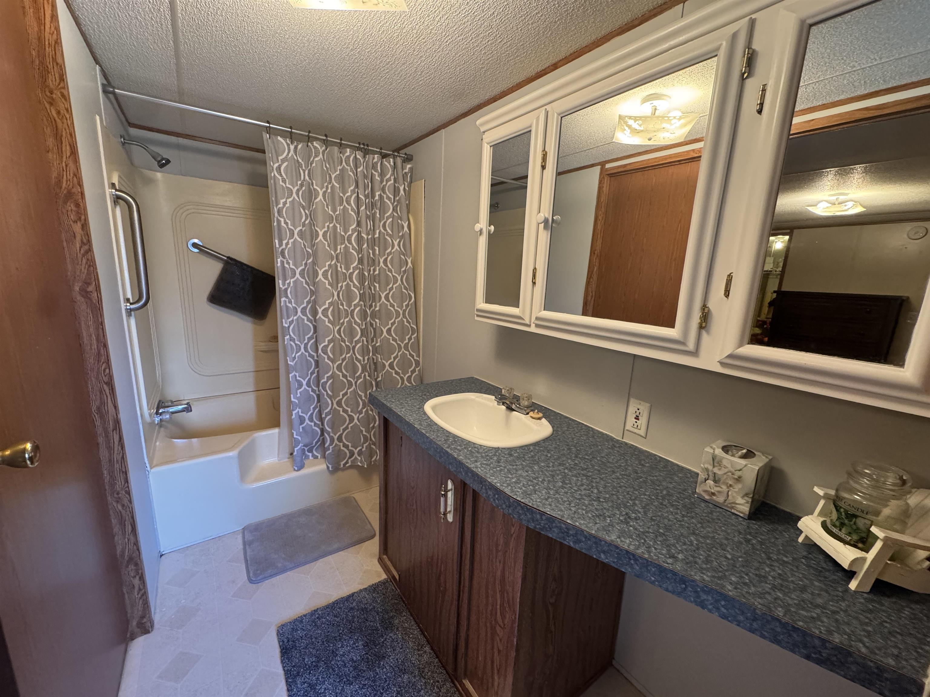 2511 Watkins Road Michie, TN 38357 - Photo 17 of 40 Full bathroom featuring a single vanity, a tub/shower combination, white wall-mounted medicine cabinets, a white drop-in sink, and wood-finish cabinetry