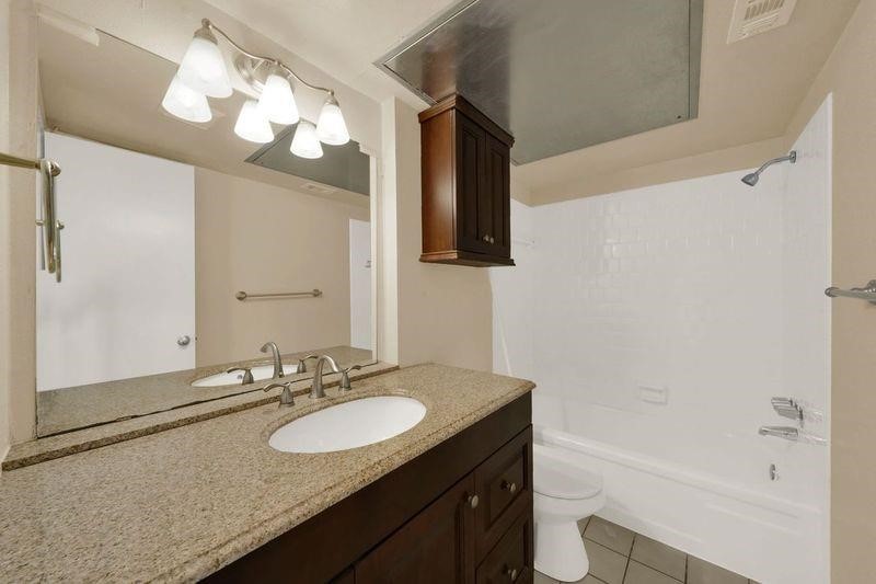 1815 Commonwealth Street, Unit D Houston, TX 77006 - Photo 12 of 23 a bathroom with a granite countertop sink a toilet a mirror a vanity and bathtub