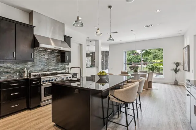 a kitchen with stainless steel appliances granite countertop a stove a refrigerator a sink a dining table and chairs with wooden floor