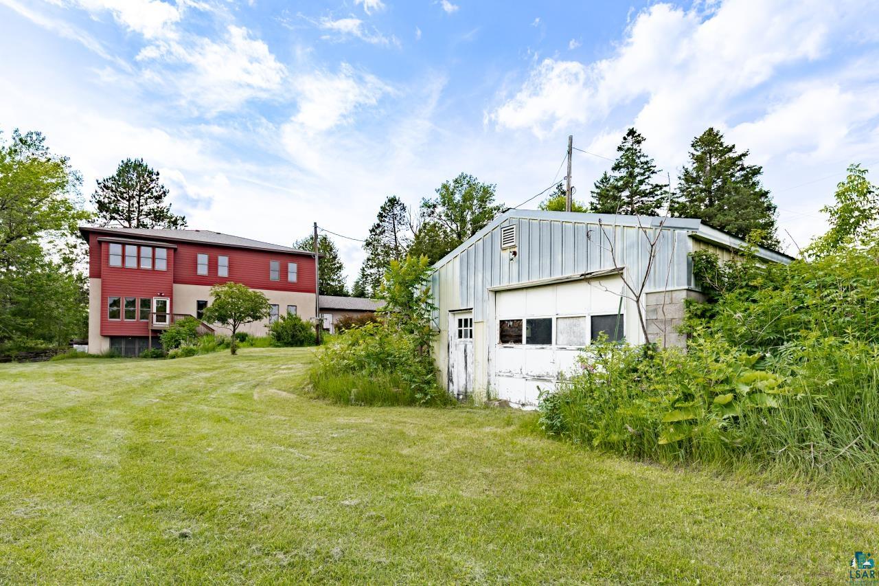 4800 Tower Road Moose Lake, MN 55767 - Photo 75 of 83 Spacious lawn area with a two-story residence featuring red siding and multiple windows, alongside a separate building with a metal roof and garage door