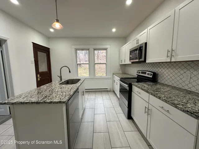 a kitchen with granite countertop a sink a counter top space cabinets and stainless steel appliances