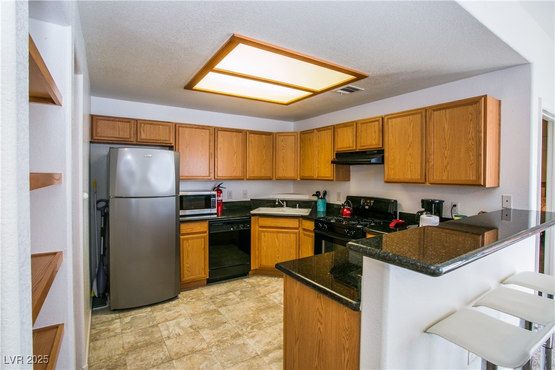 4655 Gold Dust Avenue, Unit 206 Las Vegas, NV 89120 - Photo 9 of 34 Kitchen featuring a peninsula, black appliances, brown cabinetry, dark stone counters, and a kitchen breakfast bar