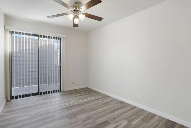 an empty room with wooden floor chandelier fan and windows