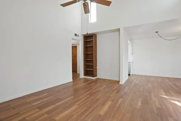 a view of an empty room with wooden floor ceiling fan
