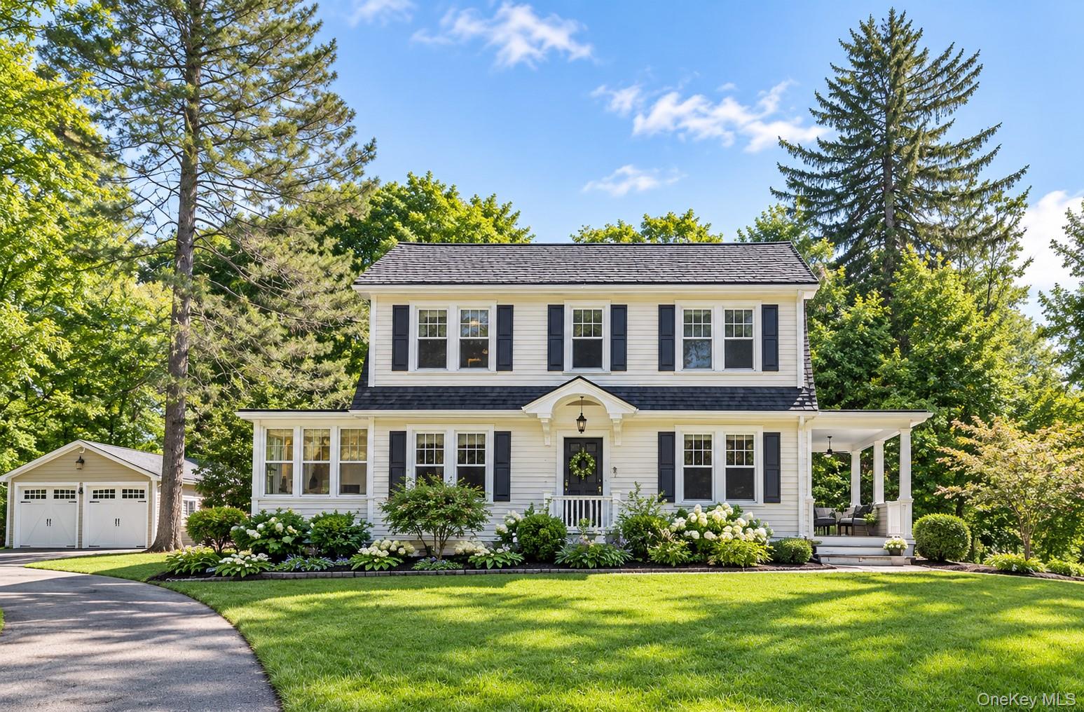 Two-story Colonial-style residence with white siding and dark shutters, featuring a covered front entry and a side porch