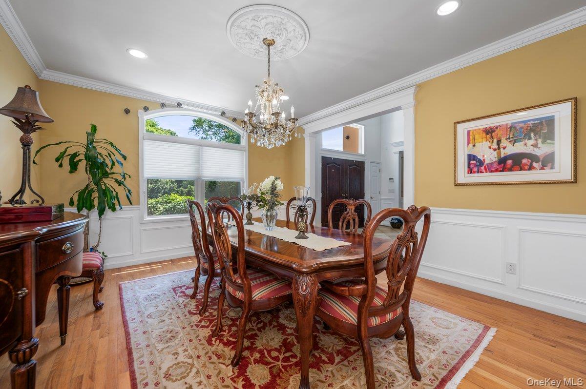 129 Round Swamp Road Huntington, NY 11743 - Photo 47 of 49 Dining room featuring hardwood flooring, an arched window, decorative wainscoting, an ornate ceiling medallion, and a crystal chandelier