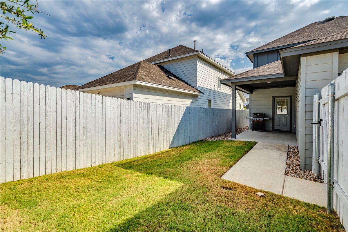 223 Rieber Road Kyle, TX 78640 - Photo 27 of 40 A wooden privacy fence encloses the grassy lawn and concrete walkway leading to the back entrance.
