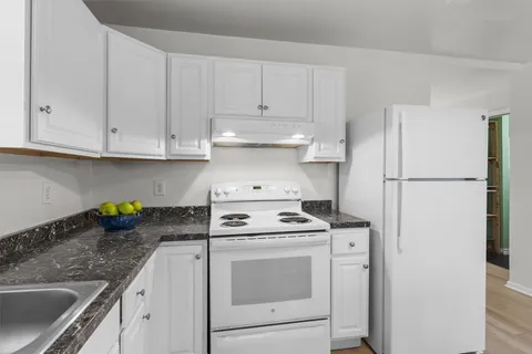 a kitchen with refrigerator a stove a granite counter tops and white cabinets