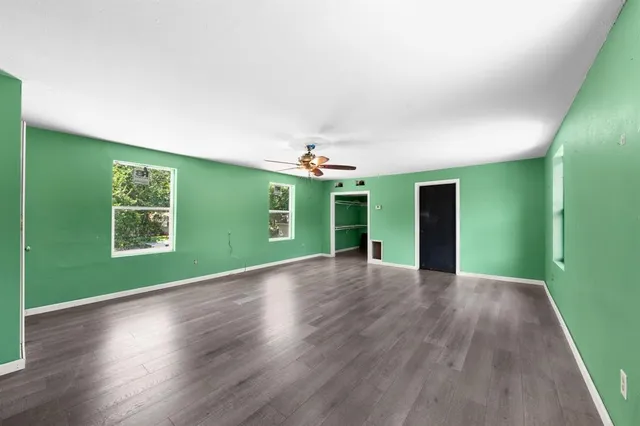 an empty room with wooden floor kitchen view and a window