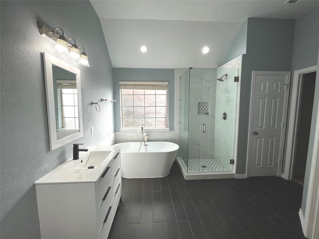 4101 White Porch Road Plano, TX 75024 - Photo 13 of 18 Master bathroom featuring dual modern vanities with integrated sinks and matte black faucets, overhead vanity lighting, dark tile flooring, and a freestanding soaking tub with a glass enclosure