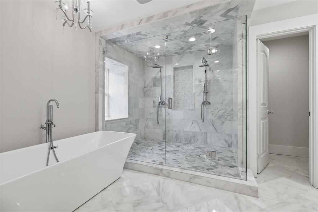 4310 Forest Bend Road Dallas, TX 75244 - Photo 21 of 40 Freestanding soaking tub with floor-mounted faucet, expansive glass-enclosed shower featuring dual shower heads, and marble-finish tile flooring