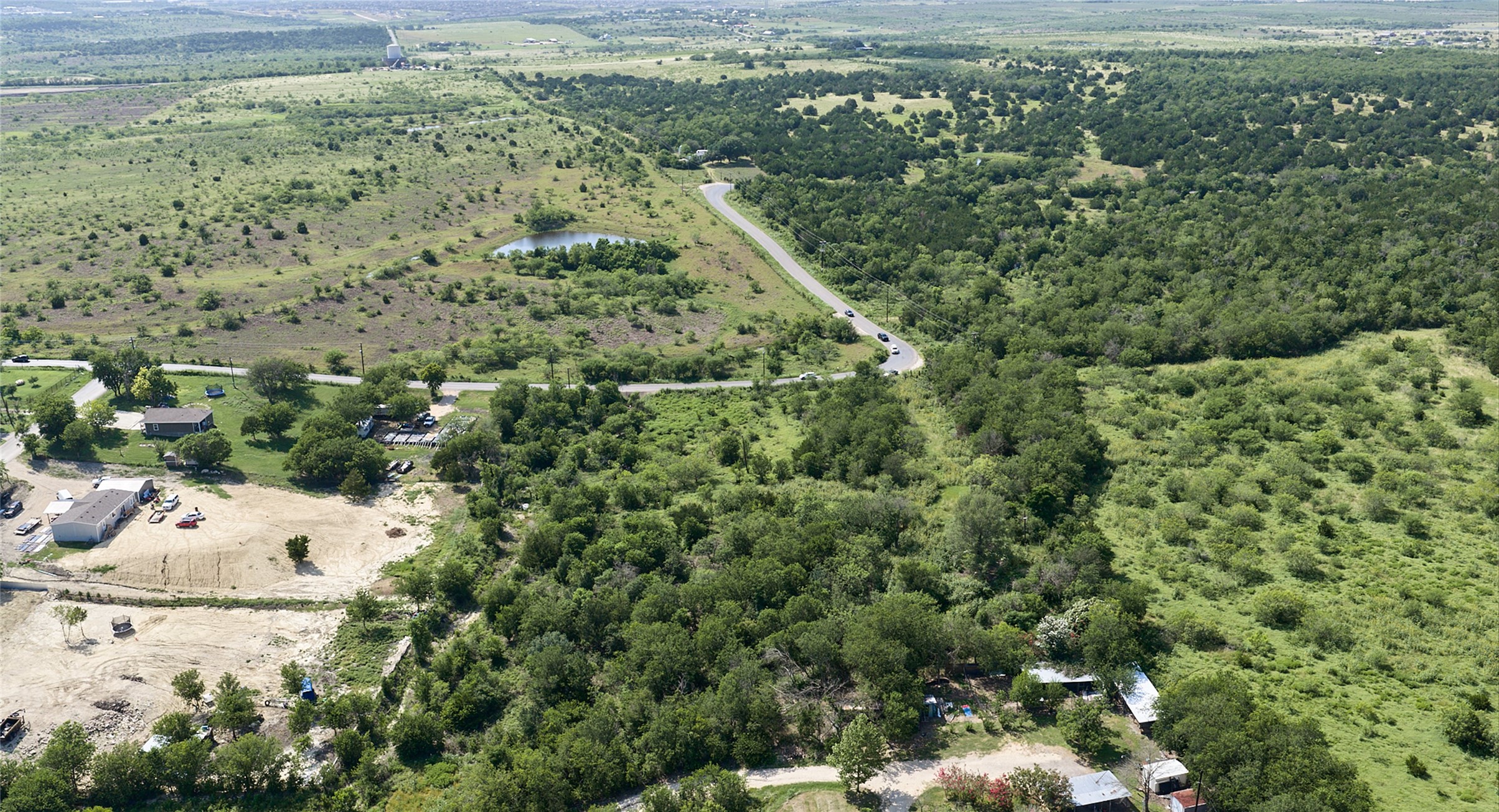 1400 Williamson Road Kyle, TX 78640 - Photo 7 of 13 Discover vast, undeveloped acreage with a winding road and distant water feature.