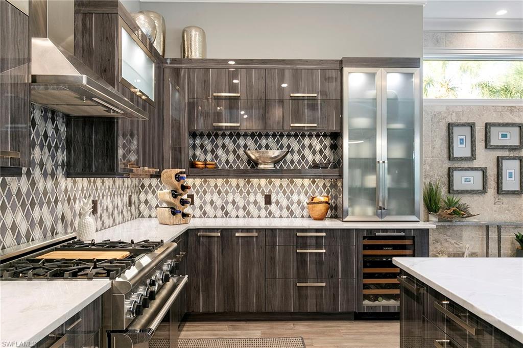927 Barcarmil Way Naples, FL 34110 - Photo 13 of 50 Bar area featuring high end stainless steel range oven, dark wood finish cabinetry, wine cooler, light stone countertops, and glass fronted cabinets