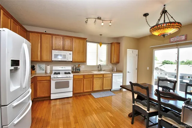 a kitchen with a sink a stove a refrigerator cabinets and a dining table with wooden floor