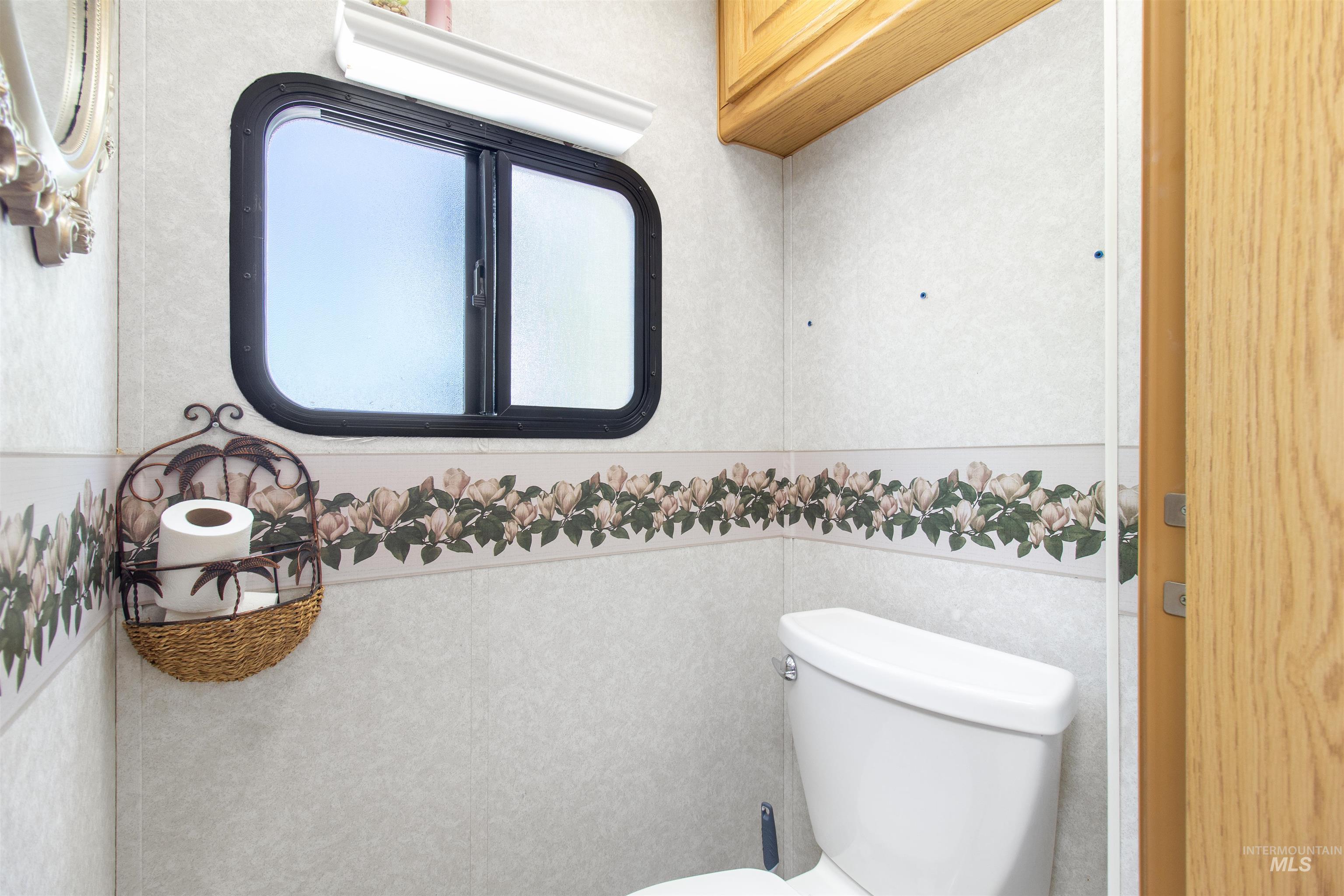 106 West Magic Road Shoshone, ID 83352 - Photo 28 of 45 Compact bathroom featuring a white toilet, window with black trim, and wood-finish cabinetry