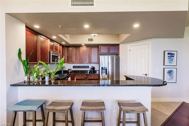 a dining room with stainless steel appliances kitchen island granite countertop a table chairs and a refrigerator