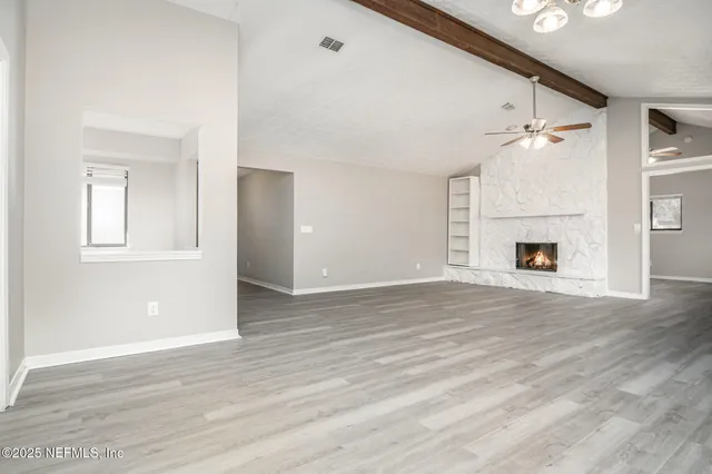an empty room with wooden floor fireplace and windows