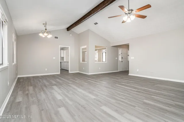 a view of an empty room with chandelier fan and wooden floor