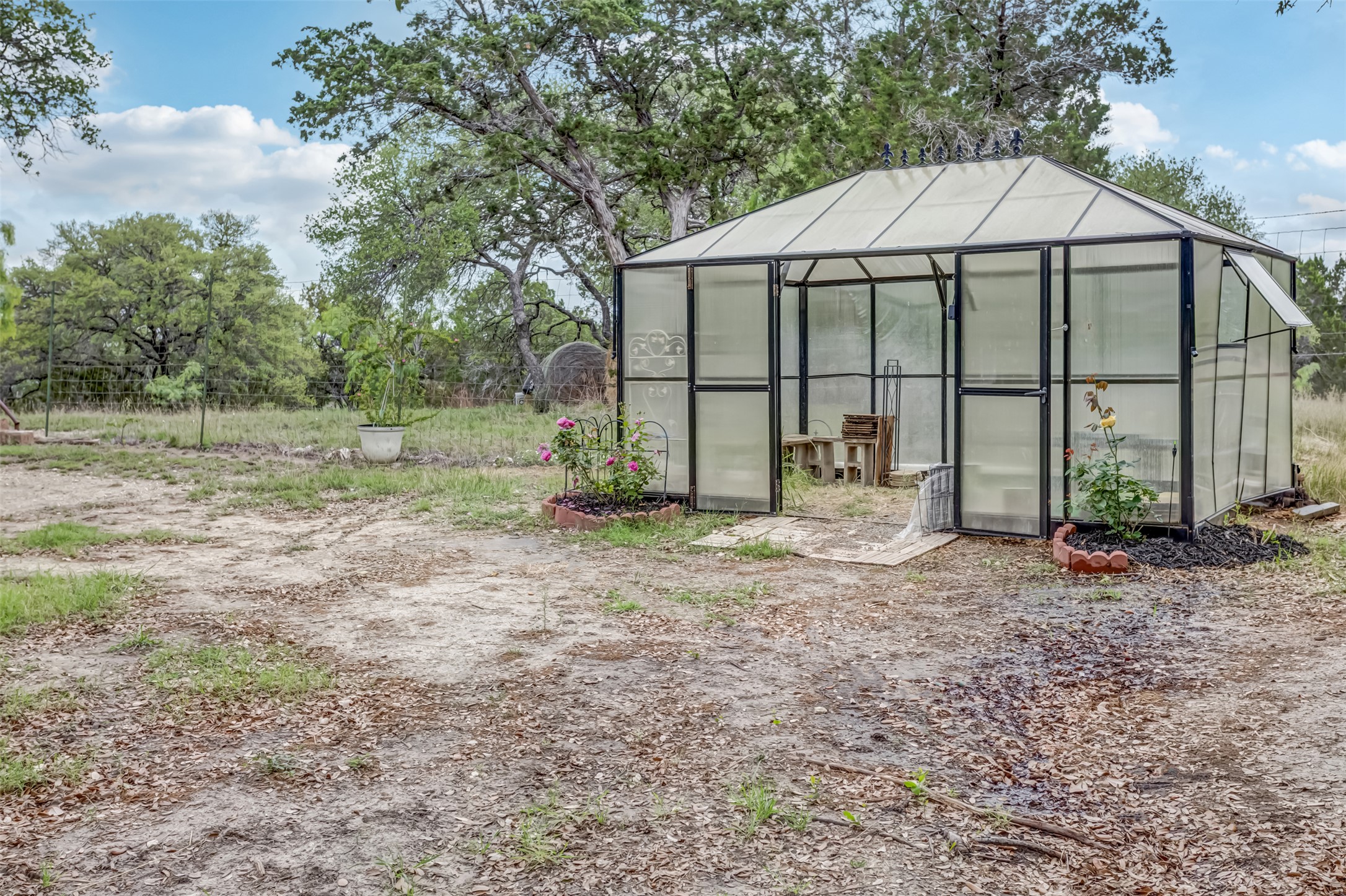4909 Lookout Ridge Drive Marble Falls, TX 78654 - Photo 38 of 39 The property includes a greenhouse with a transparent roof and walls, set within a yard featuring established trees