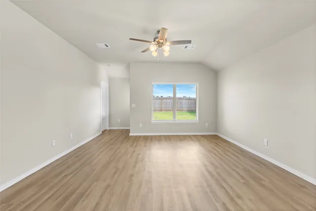 an empty room with wooden floor chandelier fan and windows