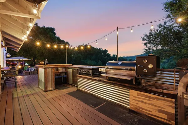 a view of a roof deck with table and chairs a barbeque with wooden floor and fence
