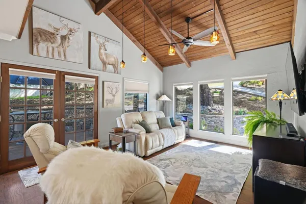 a living room with furniture two large windows and wooden floor