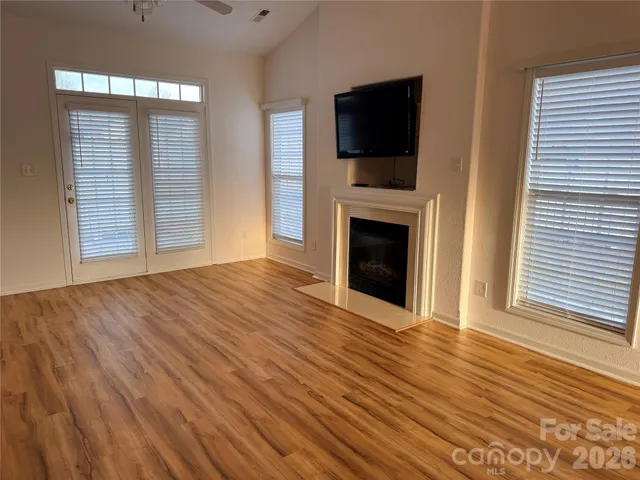 an empty room with wooden floor fireplace and windows