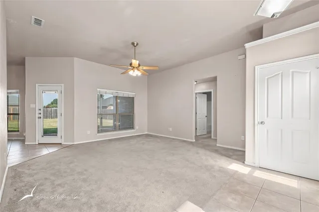 an empty room with chandelier fan and windows