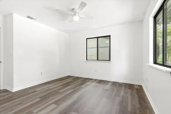 an empty room with wooden floor ceiling fan and windows