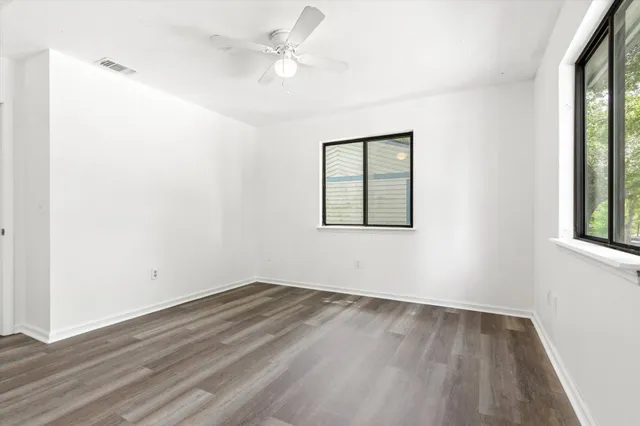 an empty room with wooden floor ceiling fan and windows