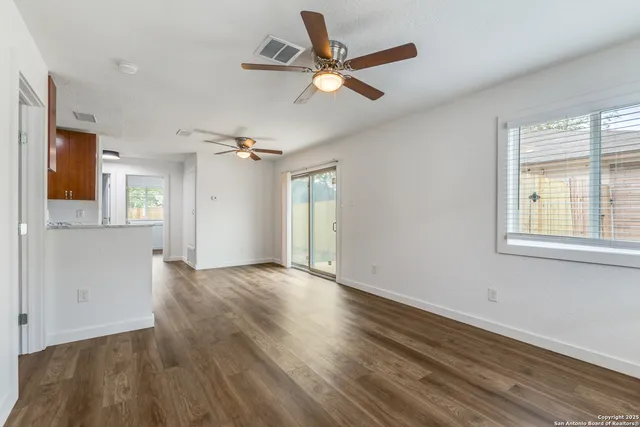 an empty room with wooden floor ceiling fan and windows