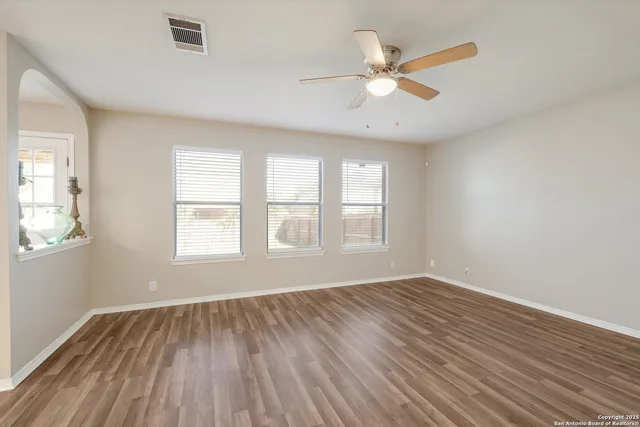 an empty room with wooden floor windows and fan