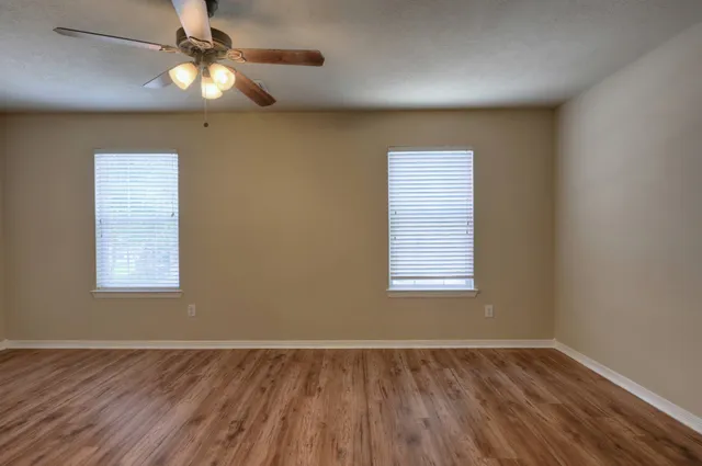 an empty room with wooden floor fan and windows