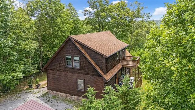 a view of a wooden house with a small yard and large trees