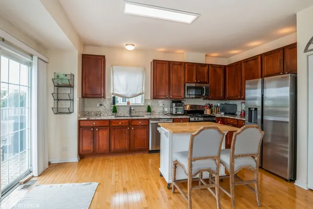 a kitchen with stainless steel appliances granite countertop wooden cabinets a refrigerator a stove a sink and a oven with wooden floor