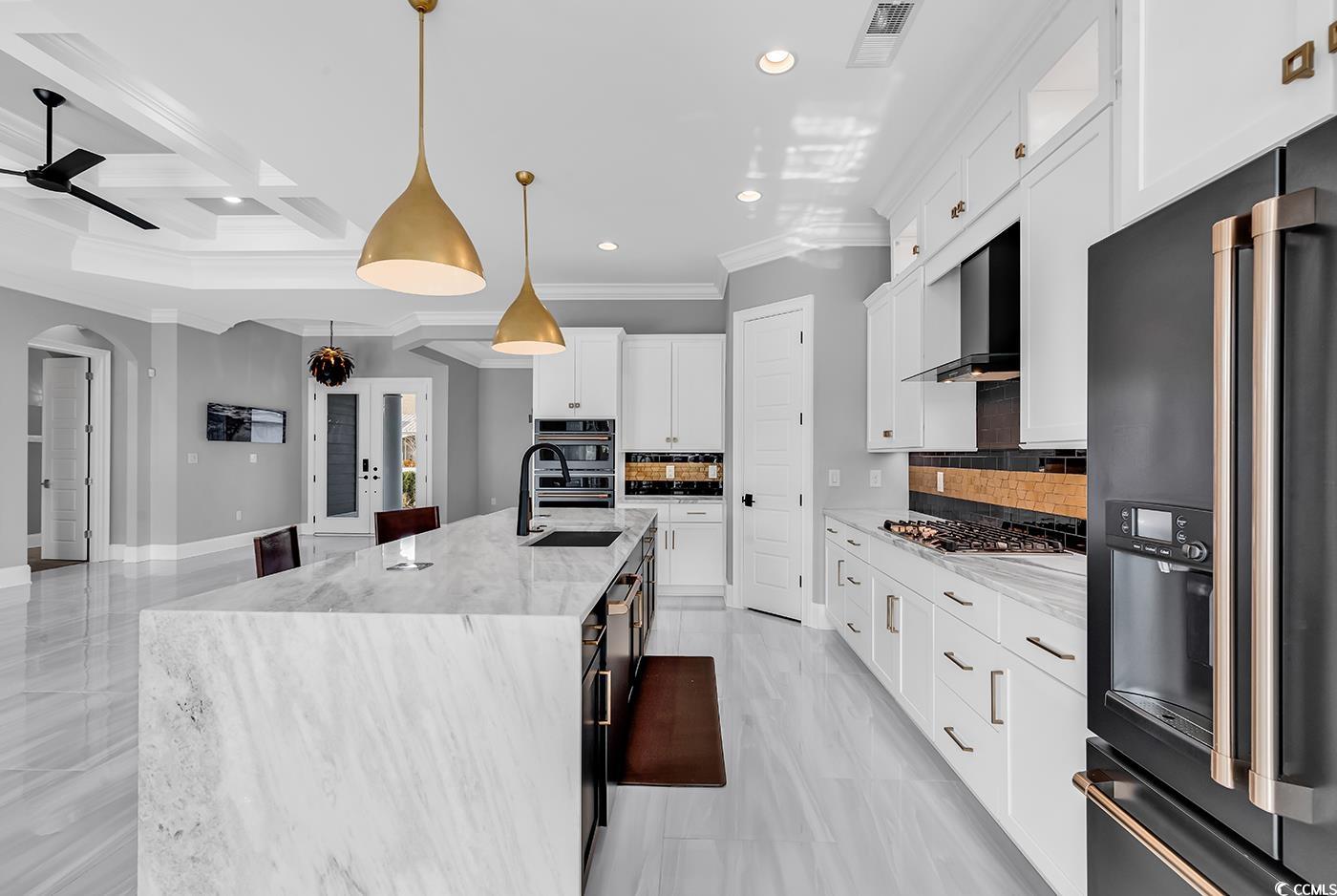 5960 Bolsena Place Myrtle Beach, SC 29572 - Photo 15 of 40 Kitchen featuring hanging light fixtures, high end black refrigerator, an island with sink, white cabinets, and wall chimney exhaust hood