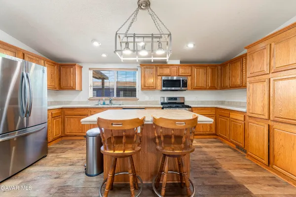 a kitchen with stainless steel appliances granite countertop a refrigerator a sink dishwasher a stove a dining table and chairs with wooden floor