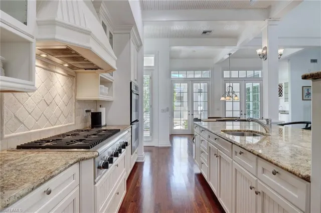 a kitchen with stainless steel appliances granite countertop a stove a sink and white cabinets with wooden floor