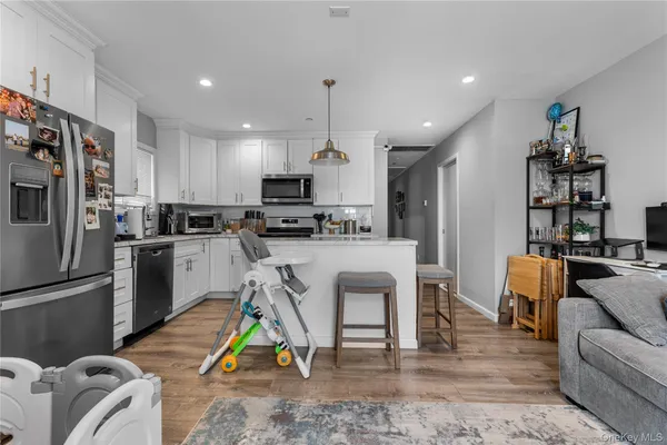 a kitchen view with stainless steel appliances kitchen island granite countertop a refrigerator a stove a oven a sink dishwasher and white cabinets with wooden floor