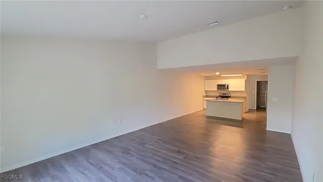 a view of empty room with kitchen view and wooden floor
