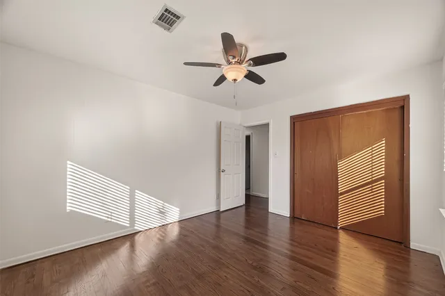 a view of an empty room with wooden floor and a ceiling fan